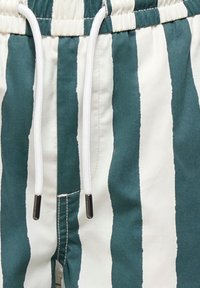Gros plan d’un tissu rayé verticalement vert et blanc avec un cordon blanc passé dans une ceinture élastique.