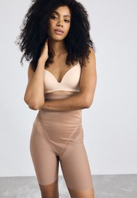 Nude sømløs BH med v-halsdesign og glatt tekstur, kombinert med høy midje shapewear. Begge i hudfarget nyanser.