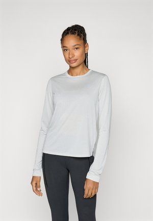 Hellgraues Langarm-Sportshirt mit gerippter Textur, rundem Ausschnitt und seitlichen Schlitzen, kombiniert mit schwarzen Leggings.