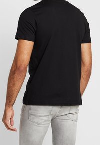 Zwarte T-shirt met korte mouwen, ronde hals en zachte stof, gecombineerd met lichtgrijze slim fit jeans met subtiele stitching op de achterzak.