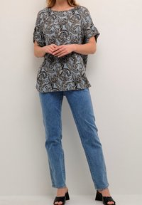 Blusa de manga corta y corte holgado con un patrón de paisley en azul, marrón y blanco, combinada con jeans rectos de tiro alto en azul claro y sandalias de tacón negras.
