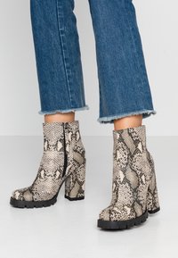 Bottines à imprimé peau de serpent avec une surface texturée, des talons épais et une fermeture éclair latérale. Semelles en caoutchouc noir et design à bout effilé.