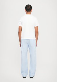 White cotton t-shirt and blue striped pants. T-shirt features short sleeves; pants are loose-fitting with large cuffs at the ankles.