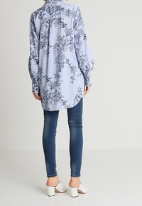 Vaaleansininen paita, jossa on valkoisia kukkakuoseja, pitkät hihat ja napitettava kaulus, yhdistettynä tummansinisiin skinny-farkkuihin ja valkoisiin korkokenkiin.