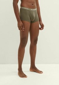 Olive green boxer shorts with a grey waistband featuring the brand name "Tom Tailor." Smooth fabric and a simple design.