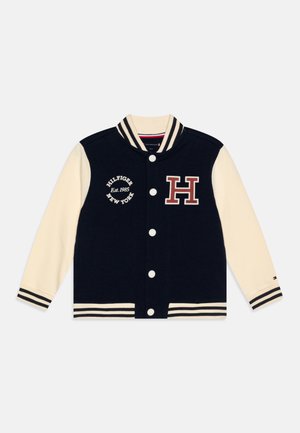 Navy and cream varsity jacket with ribbed collar, striped cuffs, snap buttons, and embroidered logo featuring "Hilfiger New York" and a large "H."