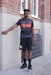 Černý sportovní dres s červenými akcenty, zdobený logem "Tezos" a znakem Manchester United. Doplňují ho černé šortky a tenisky.