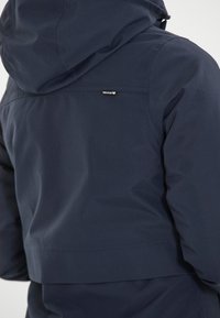 Laivaston sininen huppari, jossa on sileä ja kiiltävä pinta. Siinä on vaakasuora sauma ja pieni brändilogo takana kaula-aukon lähellä.