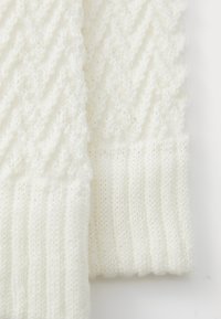 Close-up van wit gebreide stof met ribbel- en textuursgewijze kabelsteekpatronen.