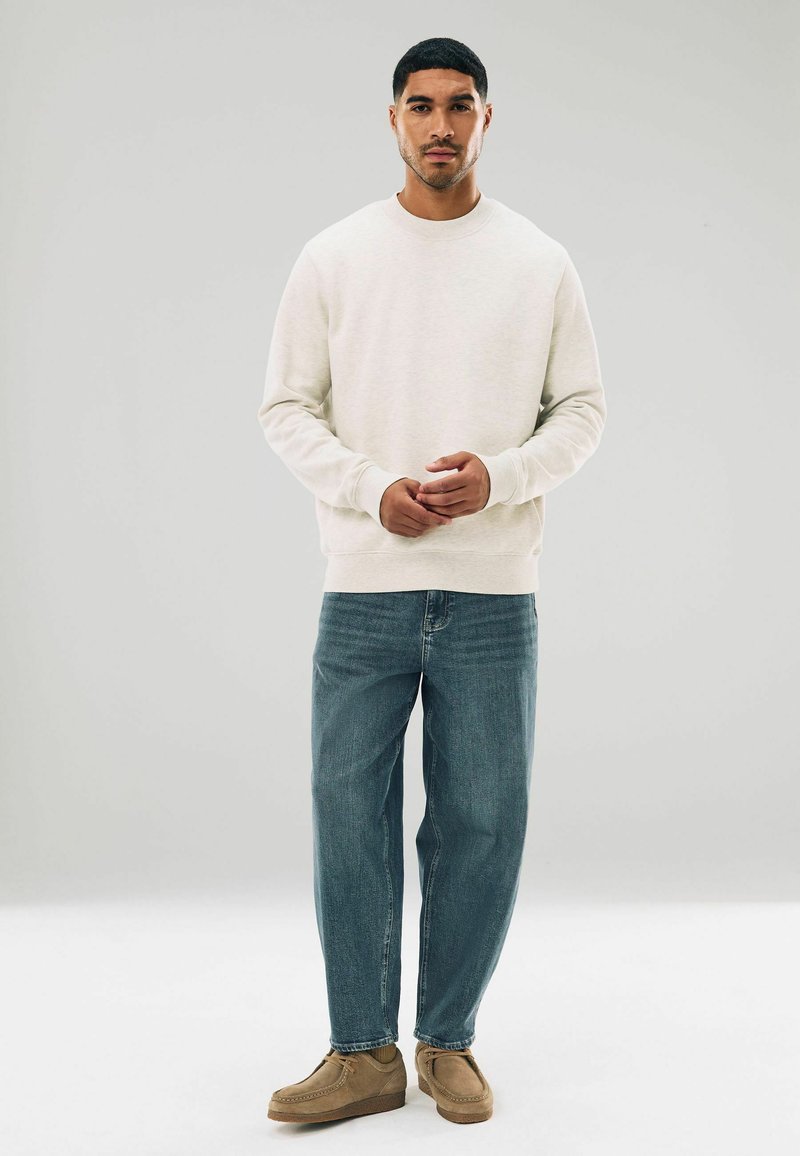 Lichtbeige sweatshirt met ribbels aan de mouwen, gecombineerd met blauwe denim jeans en brown suède schoenen. Eenvoudig ontwerp, ontspannen pasvorm.