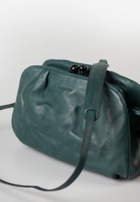 Teal Lederhandtasche mit glatter Textur, runder Form, doppeltem schwarzen Verschluss und einem langen, verstellbaren Tragegurt. Markenlogo dezent auf der Vorderseite.