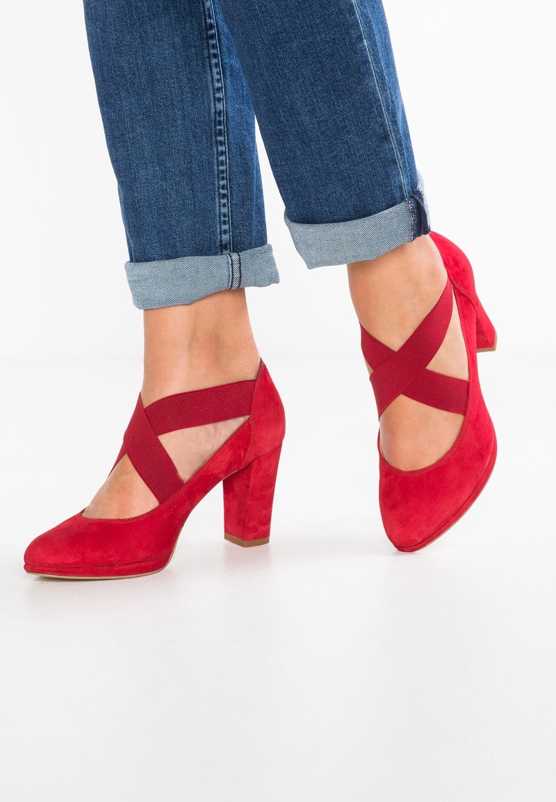 Chaussures à talons hauts en suede rouge avec un bout rond et des bretelles élastiques croisées. Les talons mesurent environ 7,5 cm de hauteur avec une finition texturée.