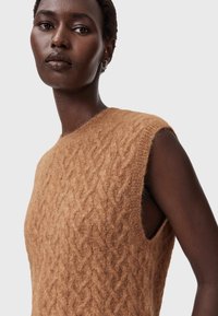 Ærmeløs strikket sweater i lysebrun med et struktureret kabelmønster, der har rå kanter ved armhullerne og blødt, fjeragtigt stof.