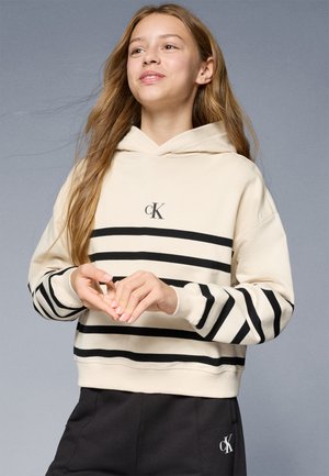 Felpa beige con strisce orizzontali nere, tasca a kangaroo frontale e logo cK sul petto. Presenta una vestibilità comoda e una texture morbida.
