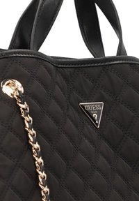 Czarna pikowana torebka ze tkaniny z elementami ze skóry, ozdobiona trójkątnym mosiężnym logo i detalami łańcuszka jako paskiem.