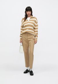 Bež i bijeli prugasti pleteni džemper s poluzip ovratnikom, uparen s hmeljnim hlačama, bijelom torbom i crnim mokasinkama sa sivim čarapama.