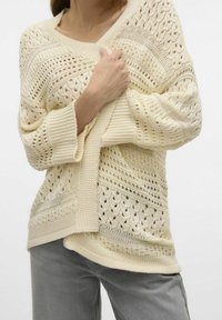 Maglione lavorato a maglia color crema con una vestibilità ampia, motivi intrecciati traforati, polsini a coste e un ampio scollo a V.