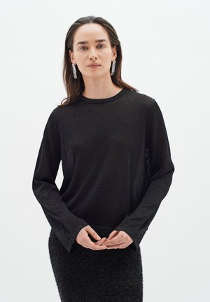 Čierny top s dlhým rukávom z priesvitnej, ľahkej tkaniny s jemným leskom. Okrúhly výstrih a voľný strih, spárovaný s textúrovanou čiernou sukňou.