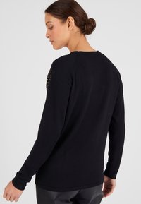 Maglione nero con maniche lunghe, caratterizzato da dettagli decorativi sulle spalle. Tessuto morbido e vestibilità rilassata, ideale per essere indossato a strati o per look casual.
