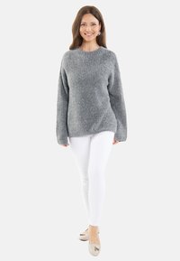 Grijze gebreide trui met lange mouwen, ronde halslijn en een ontspannen pasvorm, gecombineerd met witte slim-fit broeken en lichte flats.