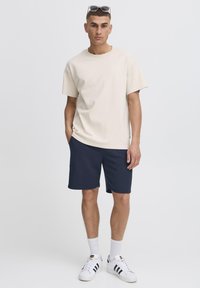 Beežist puuvillane lühikeste varrukatega t-särk, kombineeritud tumeda mereväe siniste lühikestega. Valged tossud mustade triipudega. Lihtne ja vabaaja rõivastus.