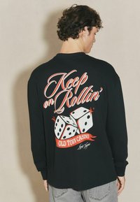 Czarna longsleeve z grafiką trzech kostek i napisem "Keep on Rollin’ Old Town Casino Las Vegas" w wyrazistych kolorach.