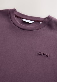 Maroonfarbenes Sweatshirt mit Rundhalsausschnitt aus weichem Stoff, mit einem dezenten, erhabenen "CPH"-Logo auf der linken Brustseite vorne.