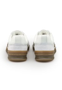 Un paio di sneaker bianche e grigio chiaro con suole spesse marroni vista da dietro su uno sfondo bianco.