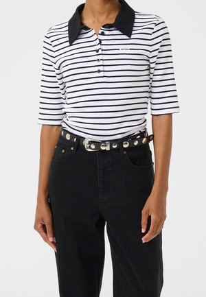Personne portant un polo rayé horizontal blanc et noir avec un col noir et un pantalon noir avec une ceinture cloutée.