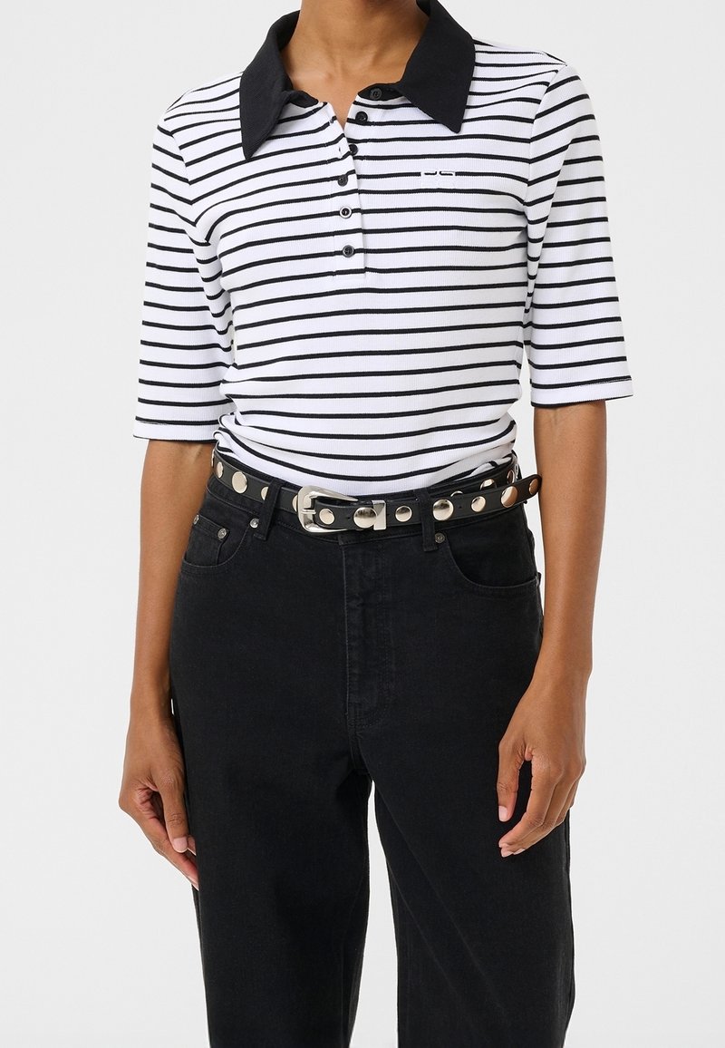Personne portant un polo rayé horizontal blanc et noir avec un col noir et un pantalon noir avec une ceinture cloutée.