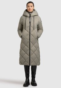 Cappotto lungo trapuntato color verde oliva con cappuccio, chiusura con zip e cordino. Presenta cuciture diagonali e due tasche laterali. Abbastanza abbinato a stivali neri.