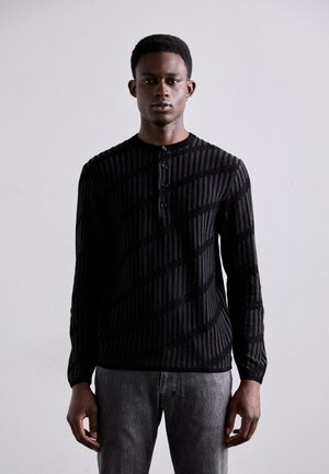 Schwarzes Langarm-Henley-Shirt mit gerippter Textur und diagonaler Streifenmuster, ausgestattet mit einer Knopfleiste und rundem Halsausschnitt.
