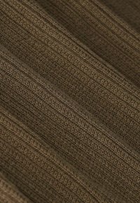 Gros plan sur un tissu tricoté marron avec une texture côtelée, montrant des motifs tissés détaillés et de légères plis diagonaux.