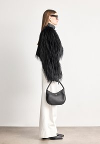 Casaco de pelagem sintética preta com fibras longas, calças brancas de perna larga e uma bolsa curva preta, complementado por óculos de sol pretos elegantes.