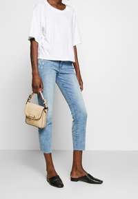 T-shirt blanc oversize, jeans bleu clair avec un ourlet effiloché, chaussures noires à enfiler en tissé, et un petit sac à main beige texturé.