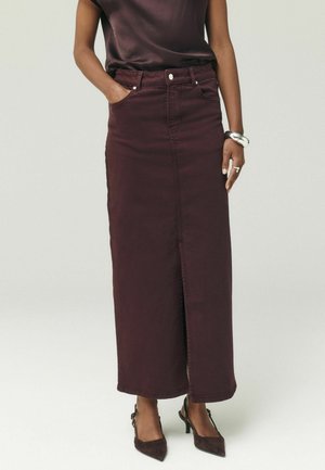 Femme portant une jupe longue maxi violet foncé avec une fente à l’avant, associée à un top assorti et des escarpins slingback à bout pointu foncés.