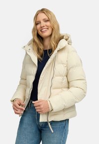 Pufferjack in lichtbeige, gemaakt van soepele stof met een rits aan de voorkant en een verstelbare capuchon. Beschikt over een aansluitend ontwerp en een doorgestikt patroon.