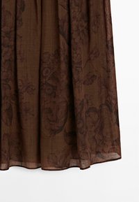 Brun tyg med ett blommönster hänger elegant, visar mjuka veck och en lätt textur som är lämplig för kläder eller inredning.
