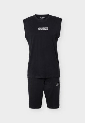 Fekete ujjatlan felső és rövidnadrág szett fehér "GUESS" logókkal a mellkason és a bal combon, egyszerű fehér háttéren bemutatva.