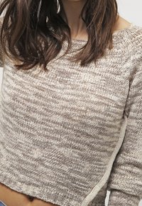 Maglione a maglia beige con un design a righe testurizzato. Presenta un ampio scollo e una vestibilità cropped con cuciture visibili lungo i bordi.
