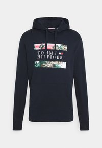 Granatowa bluza z kapturem, kieszenią z przodu, kapturem ze sznurkiem oraz tropikalnym nadrukiem z palmami i napisem "Tommy Hilfiger" wraz z logo.