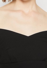 Kvinna i en axelbandslös svart klädsel, med fokus på bara axlar och övre bröstområde, samt kort brunt hår synligt.