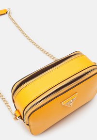 Bolso amarillo crossbody con compartimentos dobles con cremallera, material sintético texturizado, acentos en hardware dorado y una sección marrón en contraste en la parte superior.