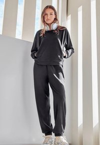 Sudadera negra y pantalones deportivos a juego, hechos de un tejido suave y texturizado. Corte holgado con puños de canalé. Combínalos con zapatillas blancas que tienen una suela con estampado.