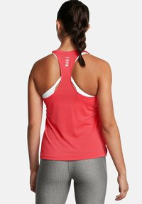 Racerback linne i ljus korall, med en texturerad tyg, en utskuren baksidedesign och vita accentdetaljer. I kombination med grå leggings.