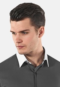 La camicia grigia con bottoni presenta un colletto bianco con dettagli a fantasia. Il tessuto liscio e la vestibilità moderna ne esaltano l'appeal visivo.