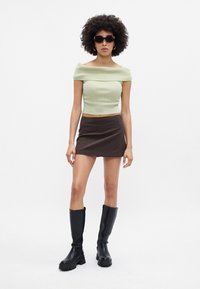 Top sin mangas de color verde menta con canalé, mini falda marrón de rayas y botas de goma negras hasta la rodilla con suelas gruesas.