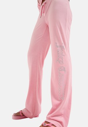 Persoon die losse roze broek draagt met "Juicy Couture" strassletters op het been en bijpassende roze sandalen.