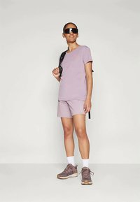 Violeta īsā piedurkne T-kreklā, kas saskaņota ar atbilstošām šortiem. Melnas saulesbrilles un mugursoma. Pelēkbrūni tenisziņi ar baltām zeķēm.