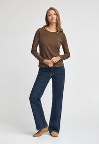 Brun långärmad tröja i mjukt material, rund halsringning, tillsammans med mörkblå vida jeans och beige ballerinas. Enkel logotypdetalj på tröjan.